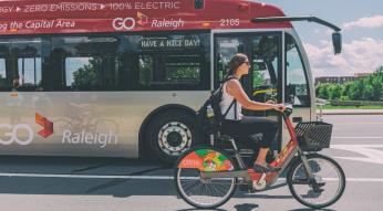 Girl riding Citrix Cycle next to GoRaleigh bus
